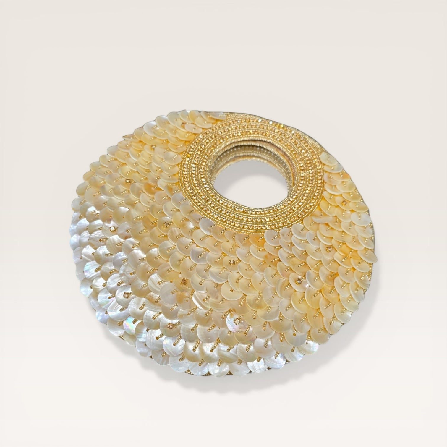 Dual-sided hand-embroidered circular mother of pearl clutch featuring a central floral shell motif with diamond-cut crystal accents and premium seed pearls. This 8.5-inch slim-profile wedding bag is crafted on a natural jute base with a hidden magnetic closure, perfect for luxury bridal and ethnic festive wear